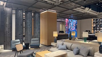 A modern hotel lobby with a sofa, chairs, a reception desk, and a large digital screen displaying a cityscape.