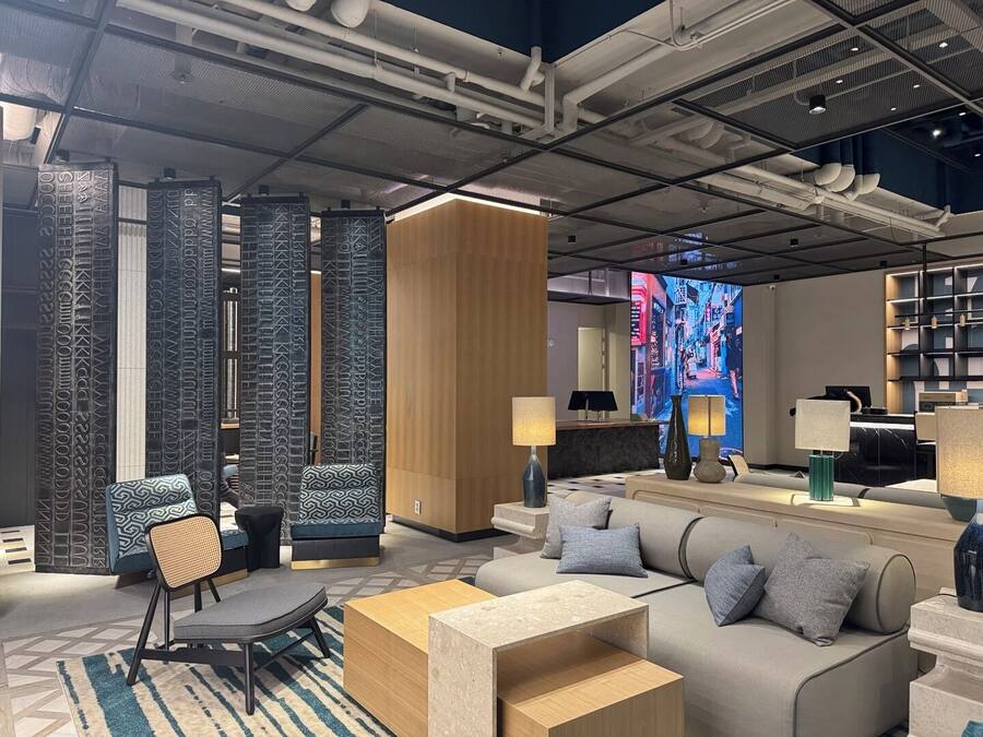 A modern hotel lobby with a sofa, chairs, a reception desk, and a large digital screen displaying a cityscape.
