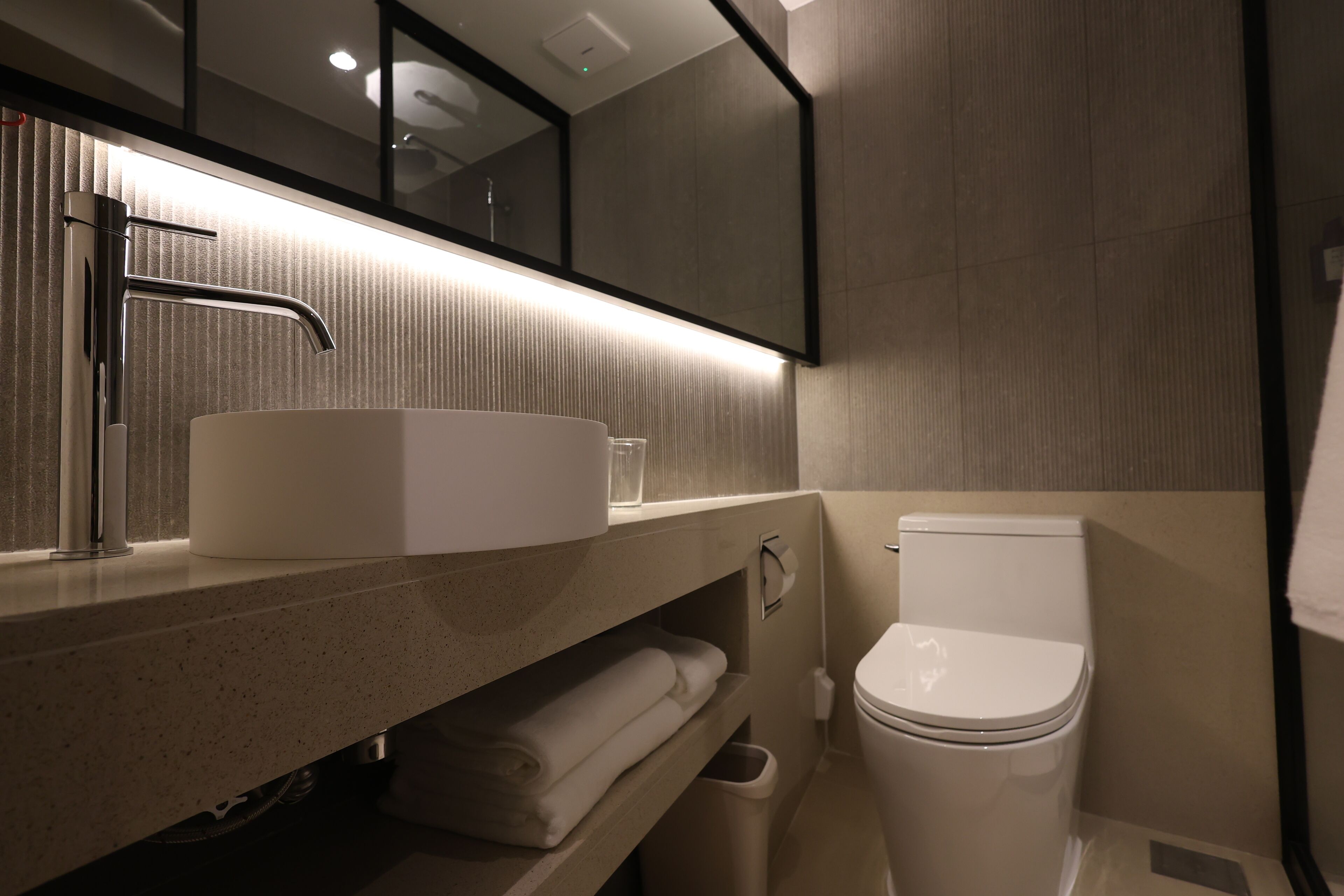 A modern bathroom with a large sink, a toilet, and a mirror above the sink.