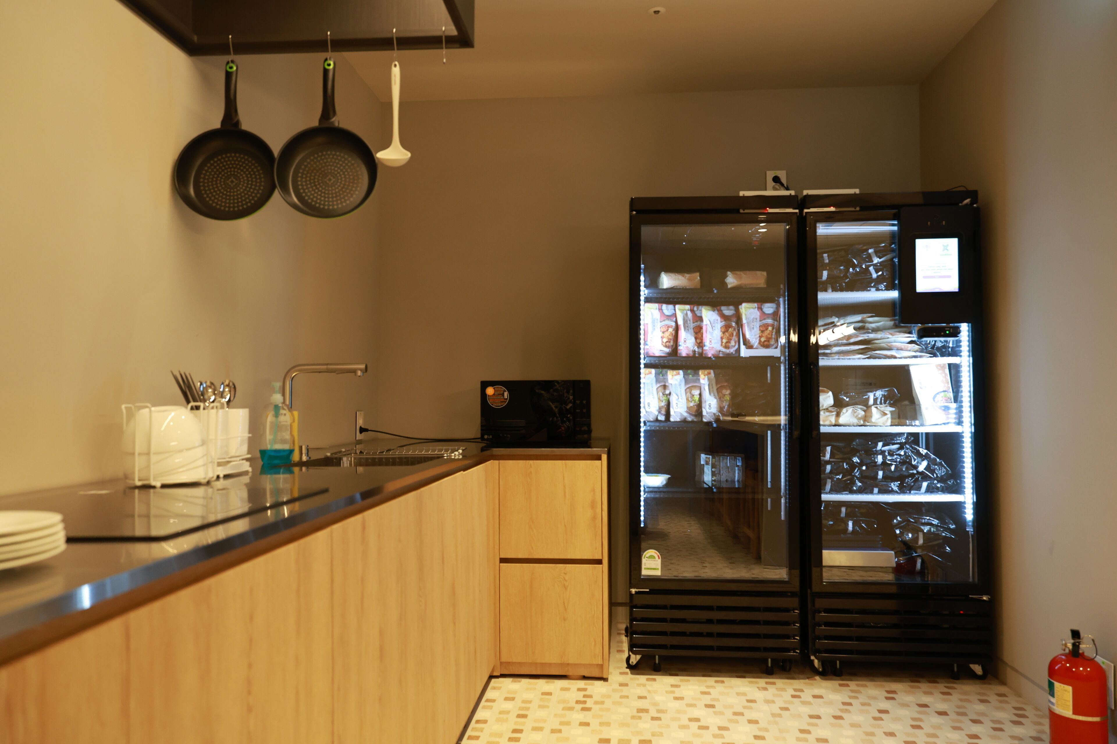 Una cocina compacta con un refrigerador negro, armarios de madera, un lavamanos y ollas colgando.