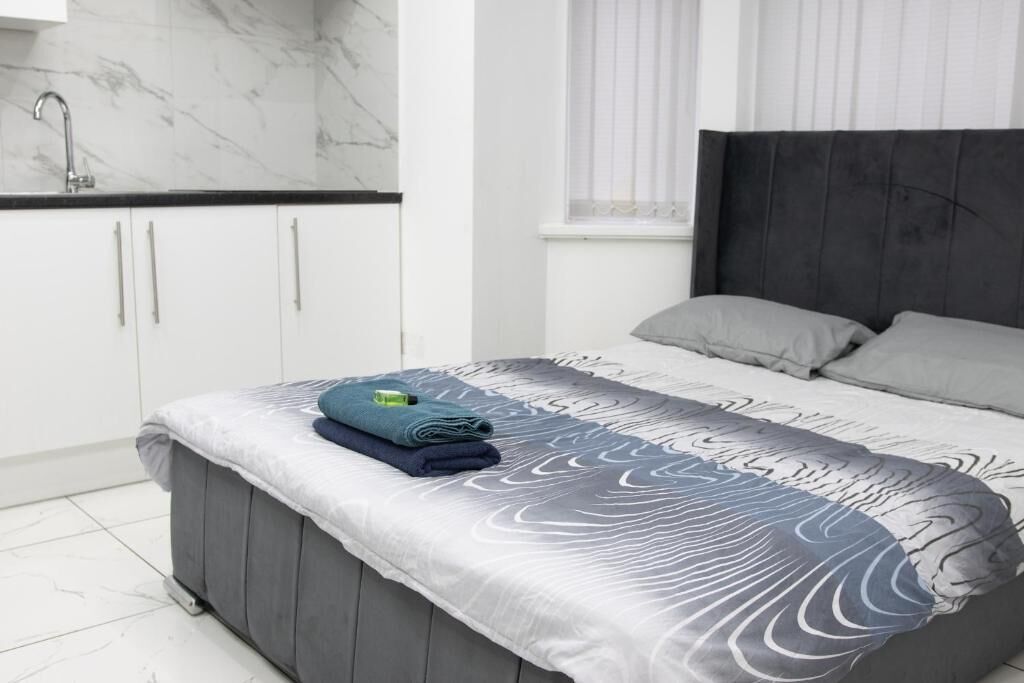 A bedroom with a bed, grey headboard, and a window with blinds.