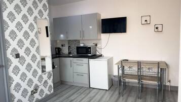 Een functionele keuken met witte kastjes, een magnetron en een kleine eettafel met stoelen.