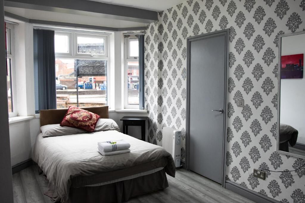 Un dormitorio con cama, mesita de noche, armario y ventana con cortinas.