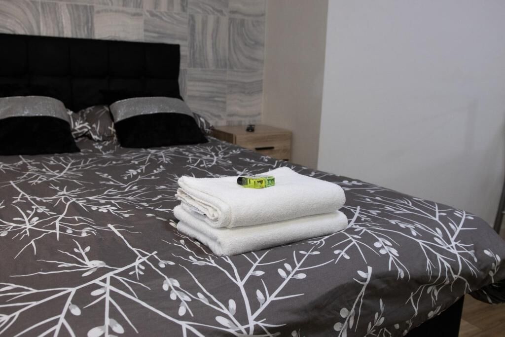 A neatly made bed with a patterned bedspread, a folded white towel, and a green object on the bed.