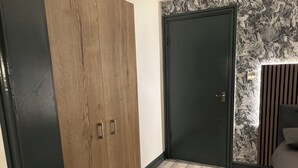 A bedroom with a wooden wardrobe, a dark door, and a bed with a striped headboard. - Hill's View Apartments (Manchester)