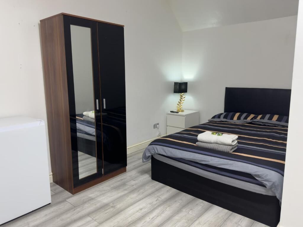 A bedroom with a bed, a wardrobe, a bedside table with a lamp, and a white bedside table.