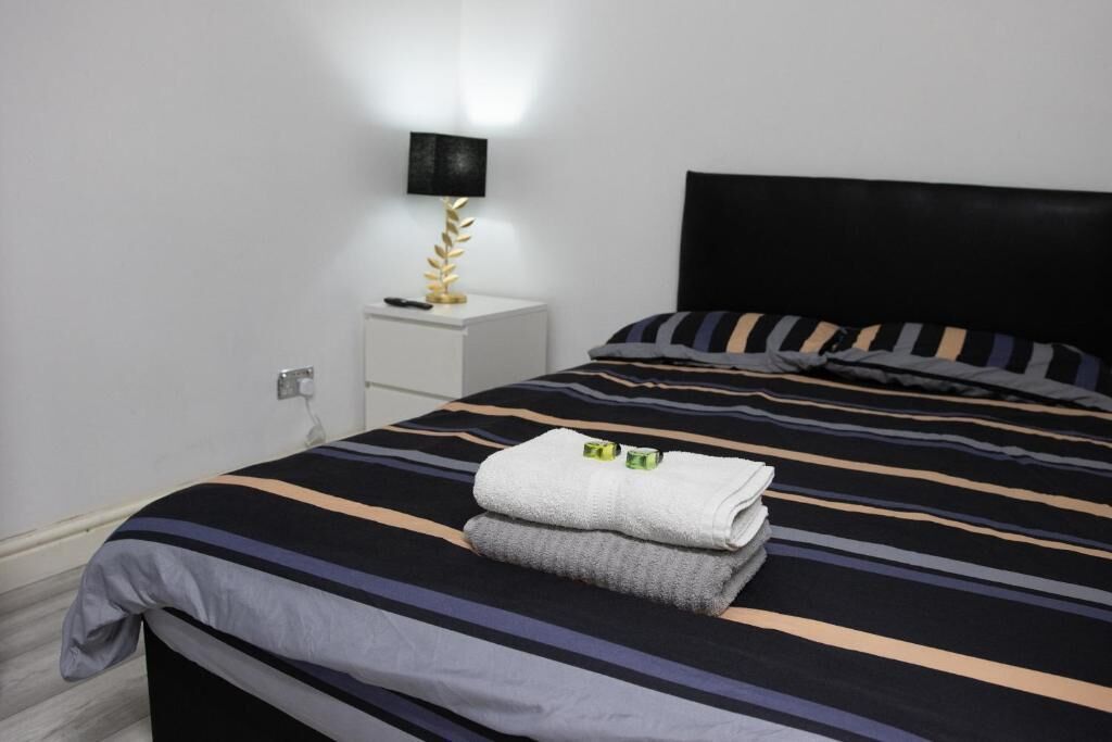 Ein ordentlich bezogenes Bett mit gestreifter Bettwäsche, eine Nachttischlampe und ein gefaltetes Handtuch auf dem Nachttisch.