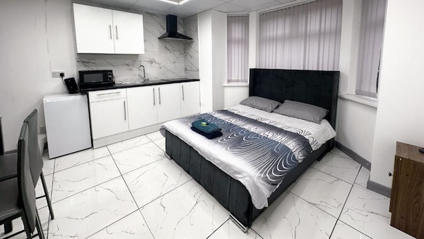 A modern bedroom with a bed, a small kitchenette, and a bathroom. - Hill's View Apartments (Manchester)