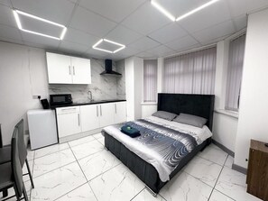 A modern bedroom with a bed, a small kitchenette, and a bathroom. - Hill's View Apartments (Manchester)