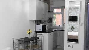A compact kitchen with white cabinets, a black countertop, and a small dining area with a metal chair and table. - Hill's View Apartments (Manchester)