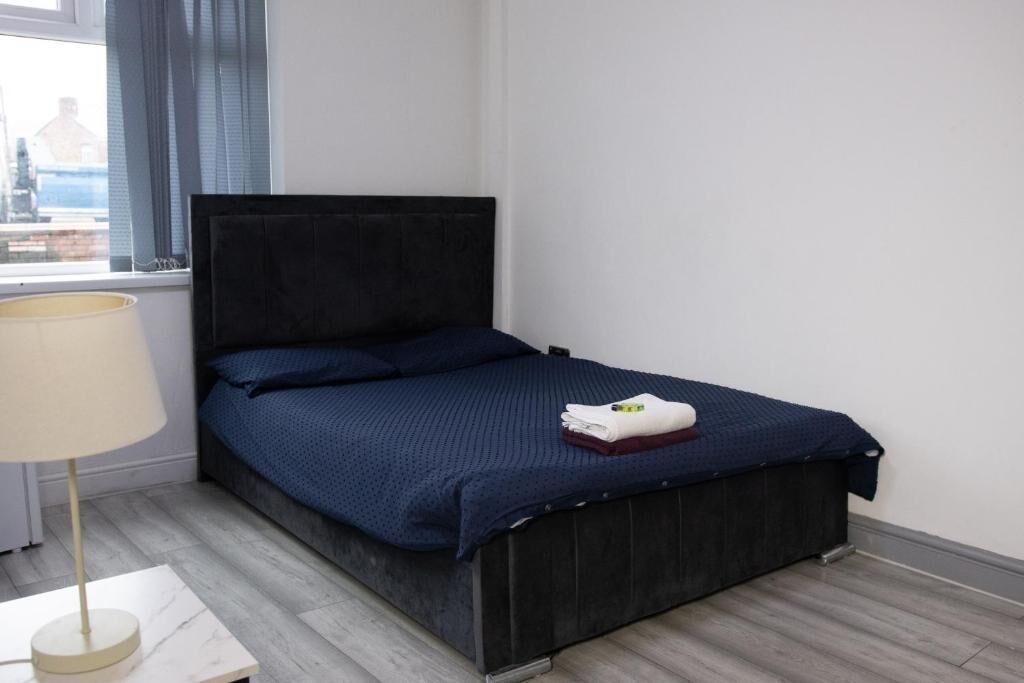 A neatly made bed with a dark headboard, a bedside lamp, and a window with curtains.