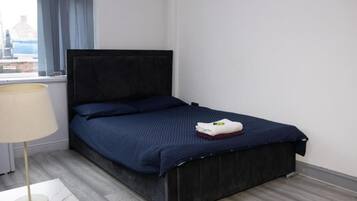 A neatly made bed with a dark headboard, a bedside lamp, and a window with curtains.