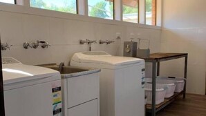 A laundry room with two washing machines, a sink, and a wooden table with laundry baskets. - Charleville Motel (Charleville)