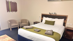 A hotel room with a large bed, two armchairs, a wooden coffee table, and a bedside table with a lamp. - Charleville Motel (Charleville)