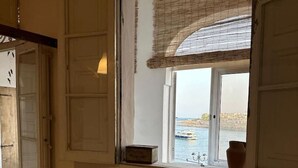 A room with a bed, a window with a view of the sea, and a door. - Ocean Pearl 2 bedroom (Wied il-Għajn)