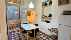 A compact kitchen with a checkered floor, a dining table with chairs, a hanging light fixture, and a refrigerator. - Ocean Pearl 2 bedroom (Wied il-Għajn)