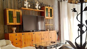 Ein Wohnzimmer mit einer Couch, einem Glastisch, Holzschränken, einem Flachbildfernseher und einer dekorativen Pendelleuchte.