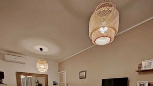 Un salon moderne avec une table ronde en bois, deux fauteuils gris, un canapé, un téléviseur et un luminaire suspendu.