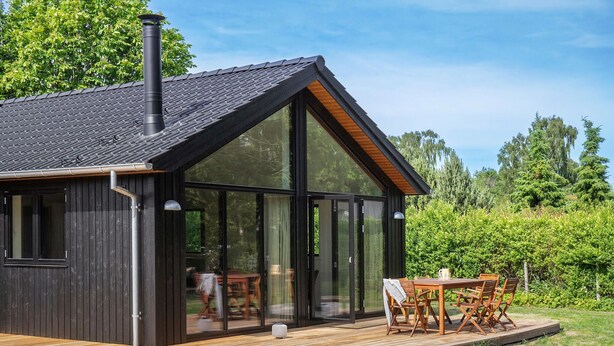 En moderne træhytte med store glasdøre, en terrasse og skorsten.