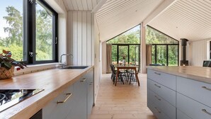 Et moderne køkken med en træbordplade, lysegrå skabe og et stort vindue med udsigt til en skov.