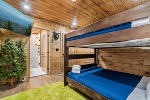 Camera con letti a castello, soffitto in legno, un piccolo albero e una decorazione a forma di testa d'orso.