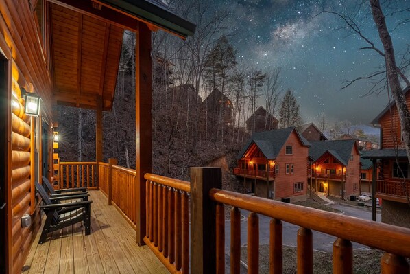 Una cabaña de madera con un porche, una terraza cubierta y vistas a otras cabañas a lo lejos.