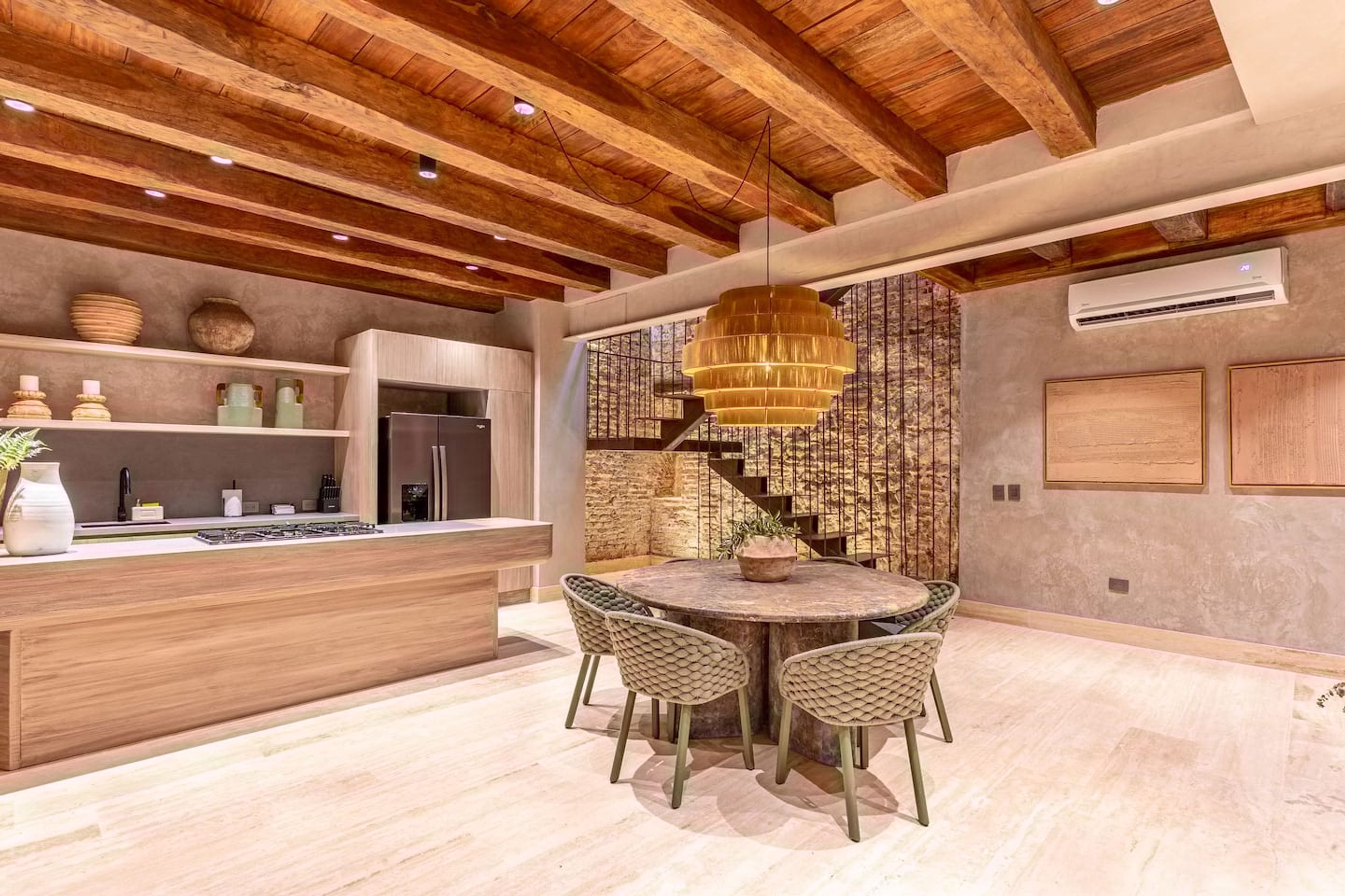 A modern kitchen with a wooden ceiling, a central island with seating, and a staircase leading to an upper level.