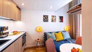 A compact living space with a kitchenette, a dining area, and a sofa with colorful cushions. - TurnKey | Angelo Roma Two Level Cozy Studio (Praha 2)