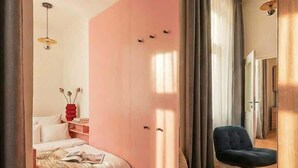 A modern bedroom with a pink wardrobe, a wooden floor, a bed with a knitted blanket, a chair, and a mirror reflecting the room. - TurnKey | Wenceslas square Loft Apartment V (Praha 1)