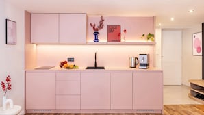 A modern kitchen with a pink cabinet, a sink, a coffee maker, and a vase with red berries.
