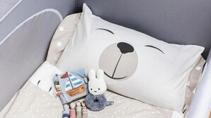 A crib with a white pillow featuring a bear face design, a small stuffed toy, and a book.