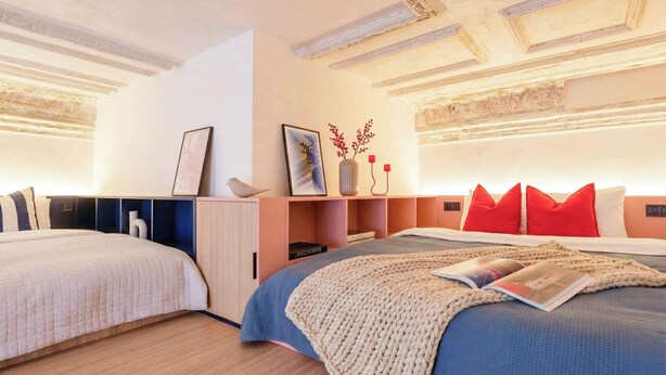 A modern bedroom with two beds, a wooden floor, and a ceiling with exposed beams.