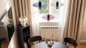 A dining area with a round table, chairs, a vase with flowers, pendant lights, a radiator, and a window with curtains. - TurnKey | Wenceslas square Two-Level Apartment V (Praha 1)