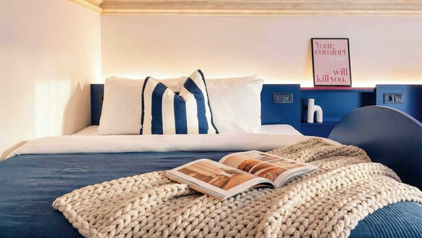 A neatly made bed with striped pillows, a knitted throw, and a magazine on the bed. - TurnKey | Wenceslas square Two-Level Apartment V (Praha 1)