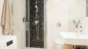 A modern bathroom with a glass-enclosed shower, a white sink, a toilet, and a washing machine. - TurnKey | Wenceslas square Two-Level Apartment V (Praha 1)