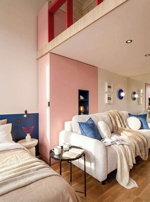 Un dormitorio moderno con techo estilo loft, un sofá blanco con detalles azules, una mesita de noche con bandeja y un pequeño estante con adornos.