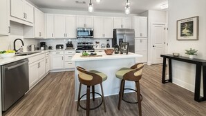 Une cuisine moderne avec des meubles blancs, des appareils en acier inoxydable et un îlot central doté de tabourets.