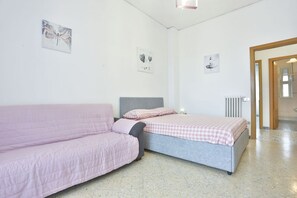 A bedroom with a pink sofa, a single bed with a checkered bedspread, and two wall-mounted artworks.