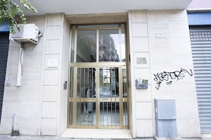 A building entrance with a glass door, a security gate, and a wall-mounted air conditioning unit.