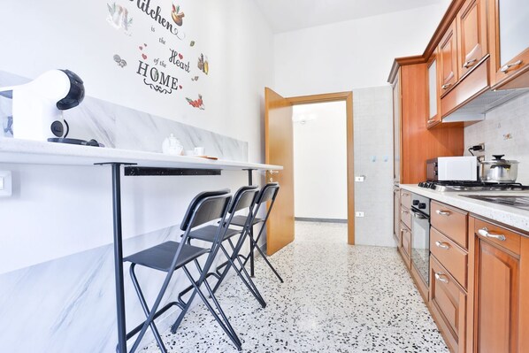 A modern kitchen with a marble countertop, wooden cabinets, a built-in oven, and a wall-mounted coffee machine.