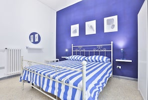 Una habitación con una cama, un radiador, un estante en la pared y una lámpara de pared.