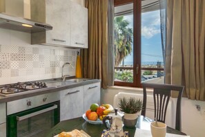 A kitchen with a gas stove, oven, and a dining area with a table, chairs, and a view of the beach.