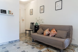 Ein Wohnzimmer mit einer Couch, einem Sessel, einer Vase mit Zweigen und gerahmten Bildern an der Wand.