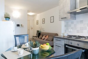A modern kitchen with a dining area, a sofa, and a coffee table with fruit. - GuestHost - Ortigia's Market Lovely Apartment (Siracusa)