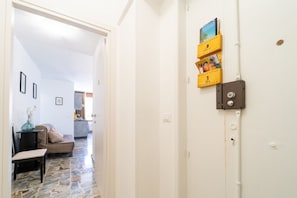 A hallway with a stone floor, a door with a lock, and a wall-mounted shelf with books.