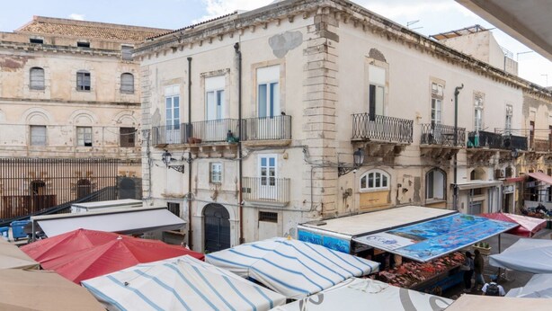 A building with multiple balconies and a street-level market area with tents.