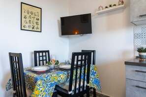A dining area with a table set for four, a flat-screen TV mounted on the wall, and a framed botanical illustration.