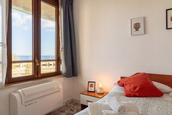 A bedroom with a bed, a nightstand, a picture frame, a radiator, and a window with curtains.