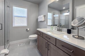 A modern bathroom with a toilet, sink, mirror, and shower.