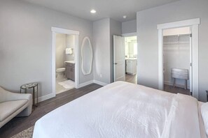 A modern bedroom with a large bed, a small side table, a chair, and a walk-in closet.